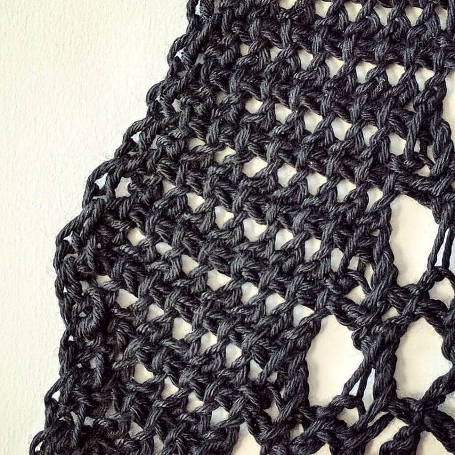 Close up of the change in stitch pattern for the collar, in progress. These are twisted Tunisian crochet stitches in DesigningVashti Lotus yarn, "Black Gleam" color. (It's inky, glossy, deep black but doesn't look like it in this lightened photo.)