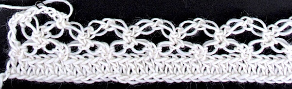 A row of love knots has been worked into a row of double crochets (an easy base). A second row of love knots is crocheted into the first row of them to create the classic lacy diamond mesh. This is a 19th cen. stitch pattern.