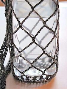 A water bottle carrier of a very open chain mesh, showing where the nearly invisible join of each round is, thanks to the tall stitch equivalent.