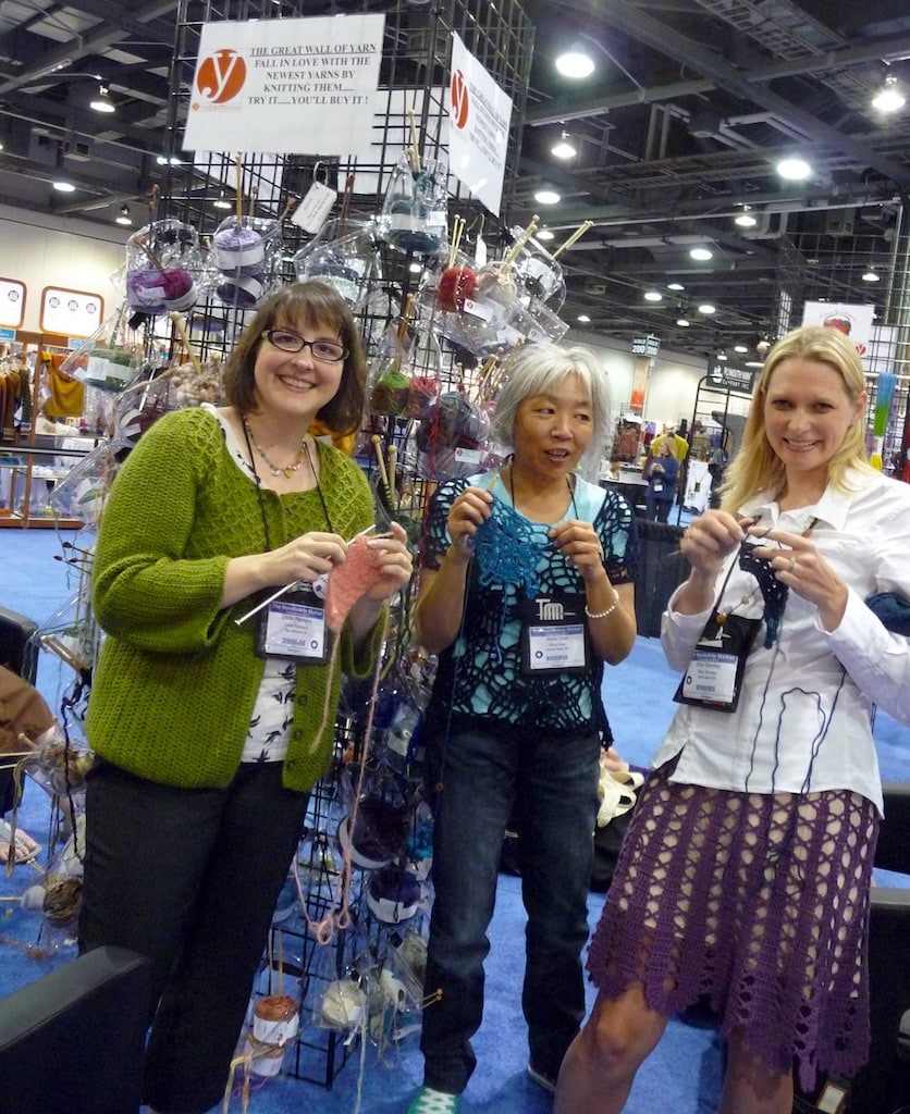 Linda Permann, Doris Chan, and Ellen Gormley using new season's yarns on the yarn wall to create crochet swatches to balance out all the knitted ones.