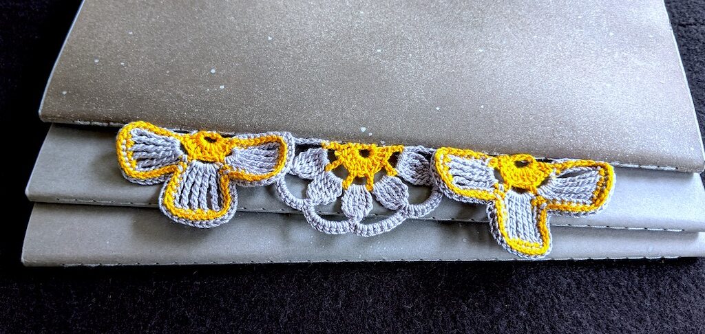 Three half-flowers in antique gold and silver colors attached to spine of large Molestine crochet notebook.